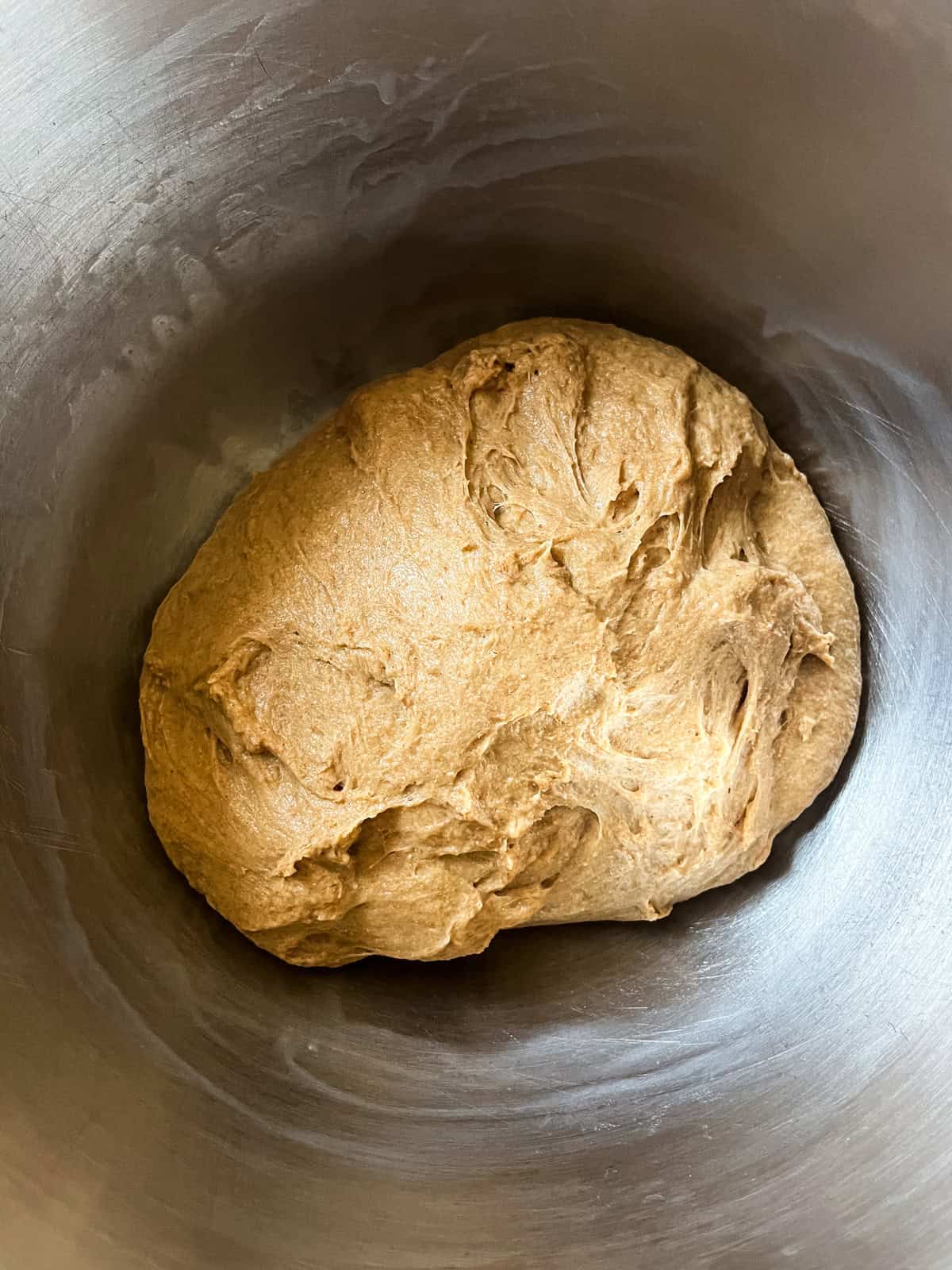 Whole grain hamburger bun dough in a smooth ball in a mixing bowl.