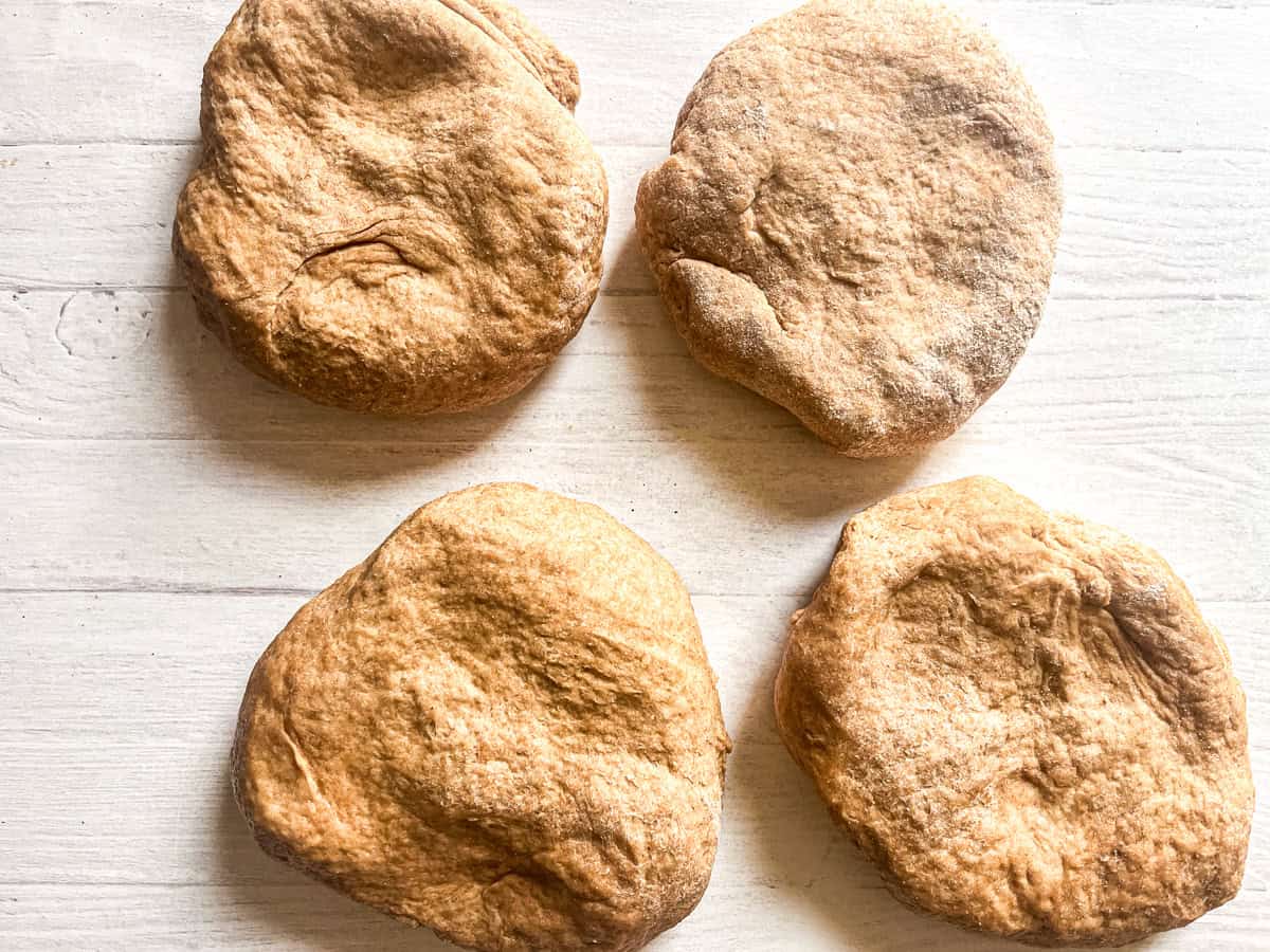 Pizza dough in four flat balls, laying on a table.