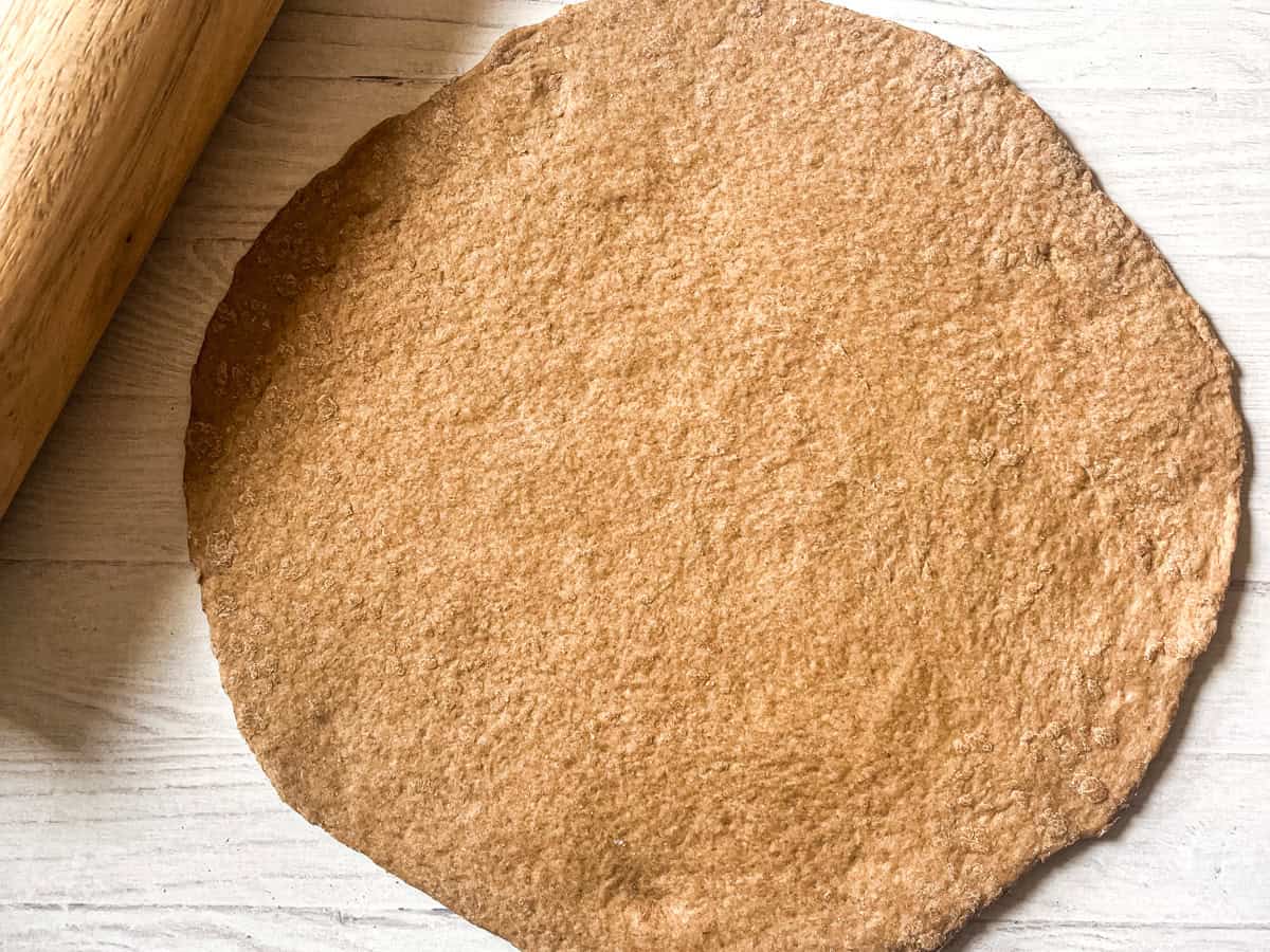 A ball of pizza dough rolled out into a flat circle next to a rolling pin.