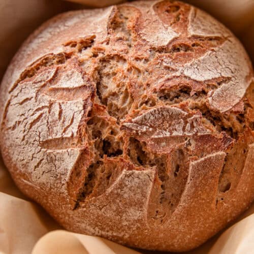 A loaf of whole grain artisan bread in a nest of parchment paper.