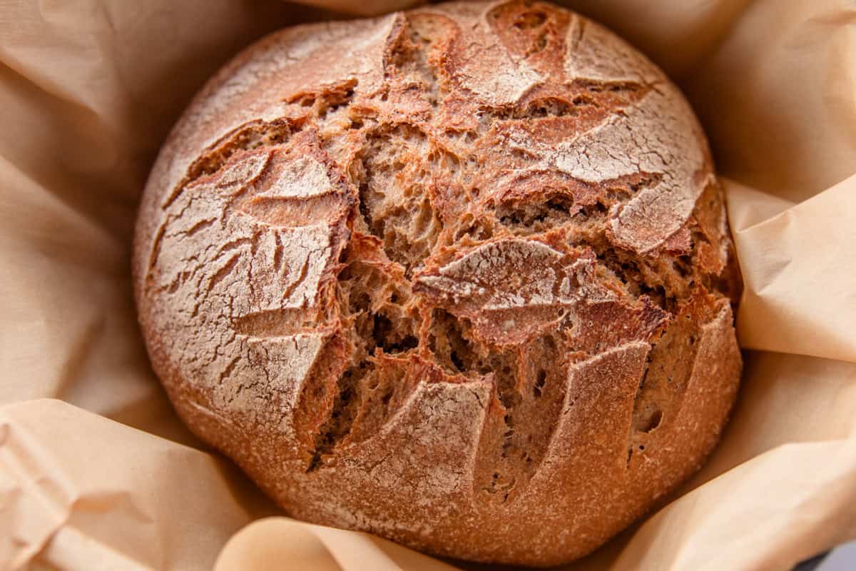 A loaf of whole grain artisan bread in a nest of parchment paper.