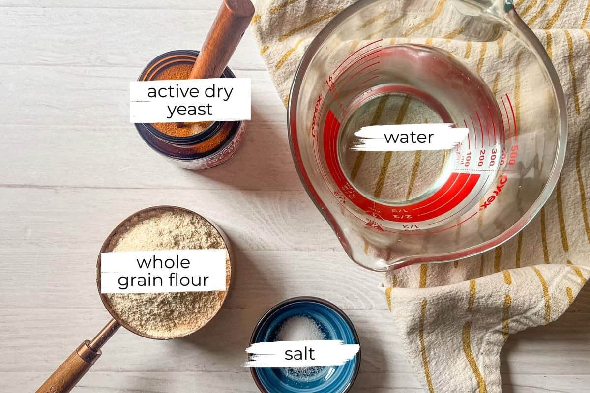Whole grain artisan bread ingredients assembled on a white table with a towel.