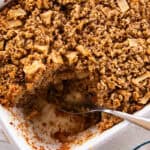 Apple Cinnamon Oatmeal Bake in a white baking dish, with a single serving taken out using a metal spoon