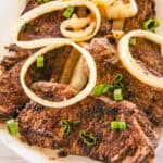 Beef liver cooked with onions on top on a white plate.