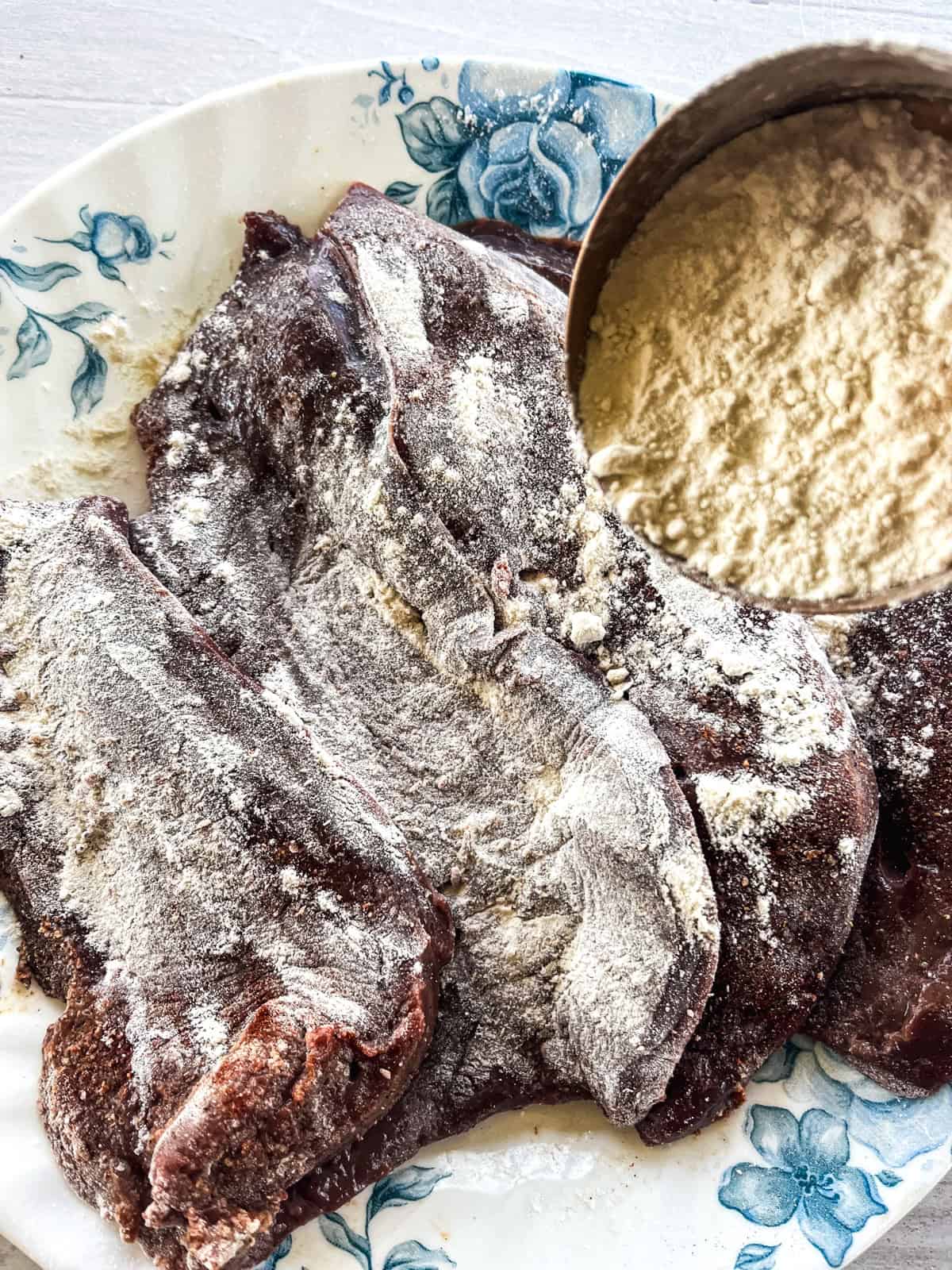 Sprinkling flour over raw beef liver on a plate.