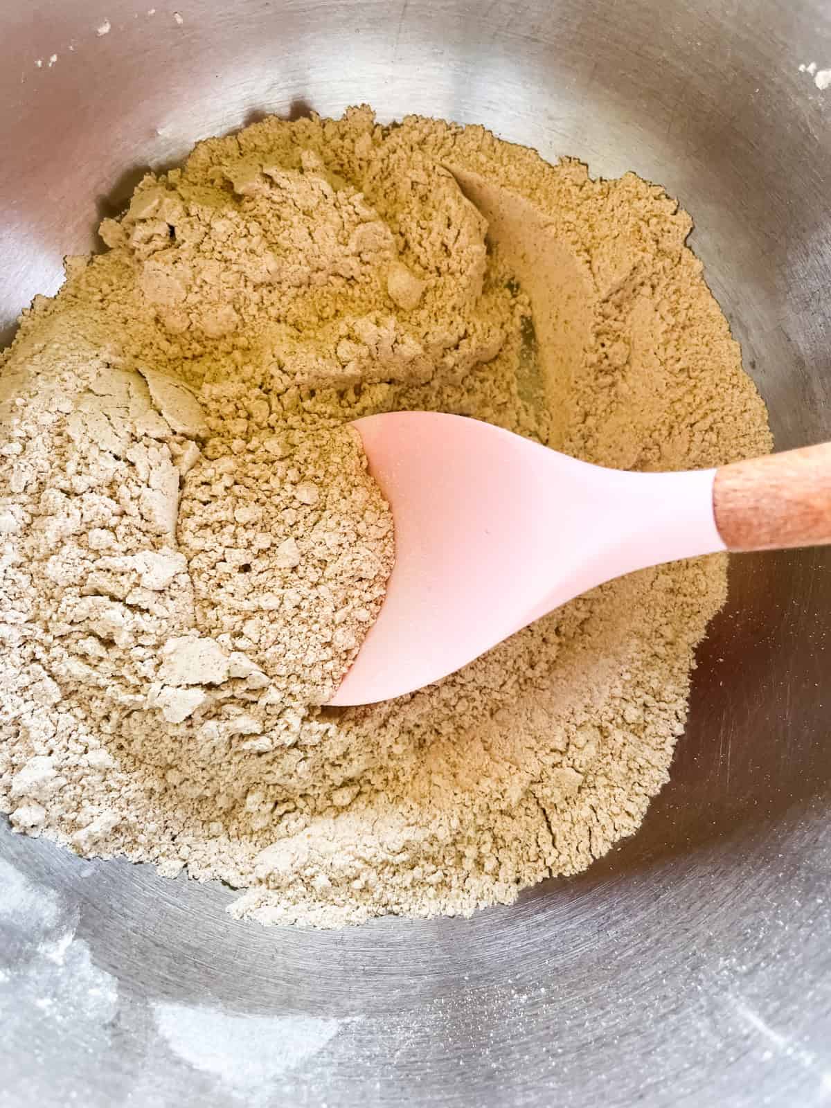 Dry ingredients for biscuits in a metal mixing bowl with a spoon.
