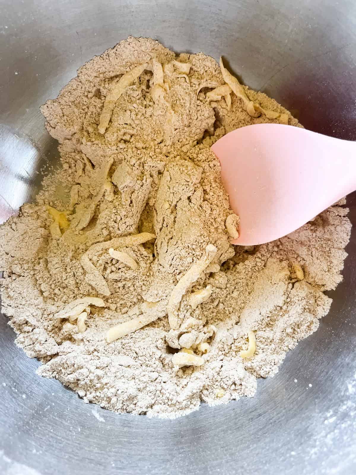 Grated butter being mixed into the dry ingredients in a metal mixing bowl.