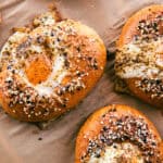 Several everything bagels on parchment paper, each with eggs cooked into their center holes.