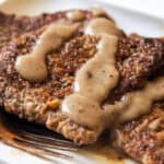 Venison cube steak on a white plate with gravy on top.