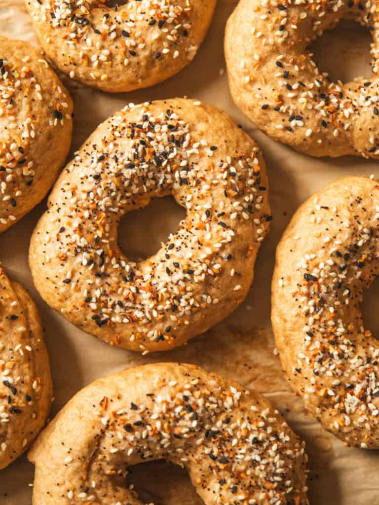 Whole grain bagels topped with everything seasoning on a piece of parchment paper.