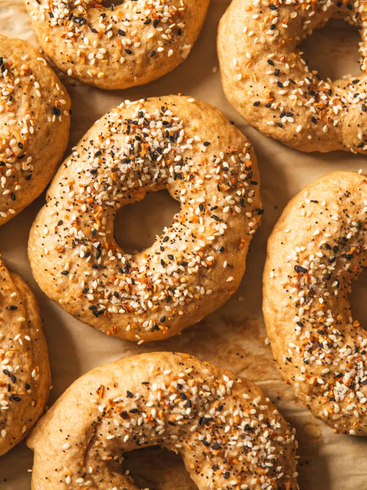 Whole grain bagels topped with everything seasoning on a piece of parchment paper.