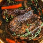 An arm roast in a pot with carrots and fresh thyme.
