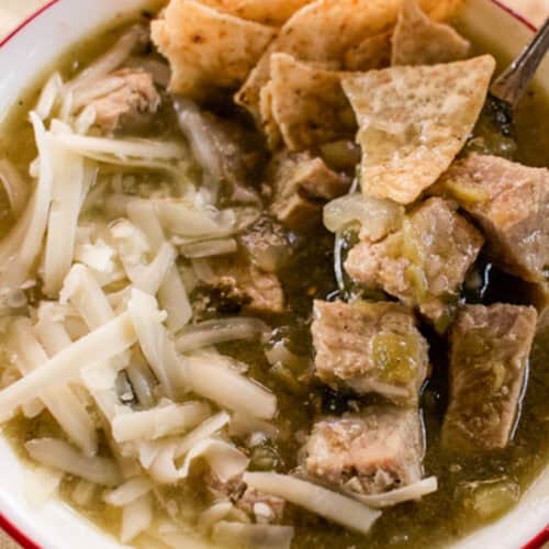 A bowl of Colorado Green Chili topped with cheese and tortilla chips.