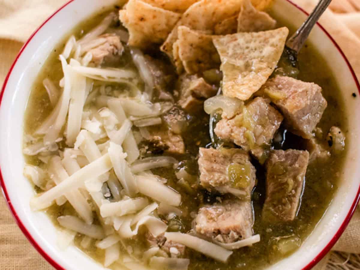 A bowl of Colorado Green Chili topped with cheese and tortilla chips.