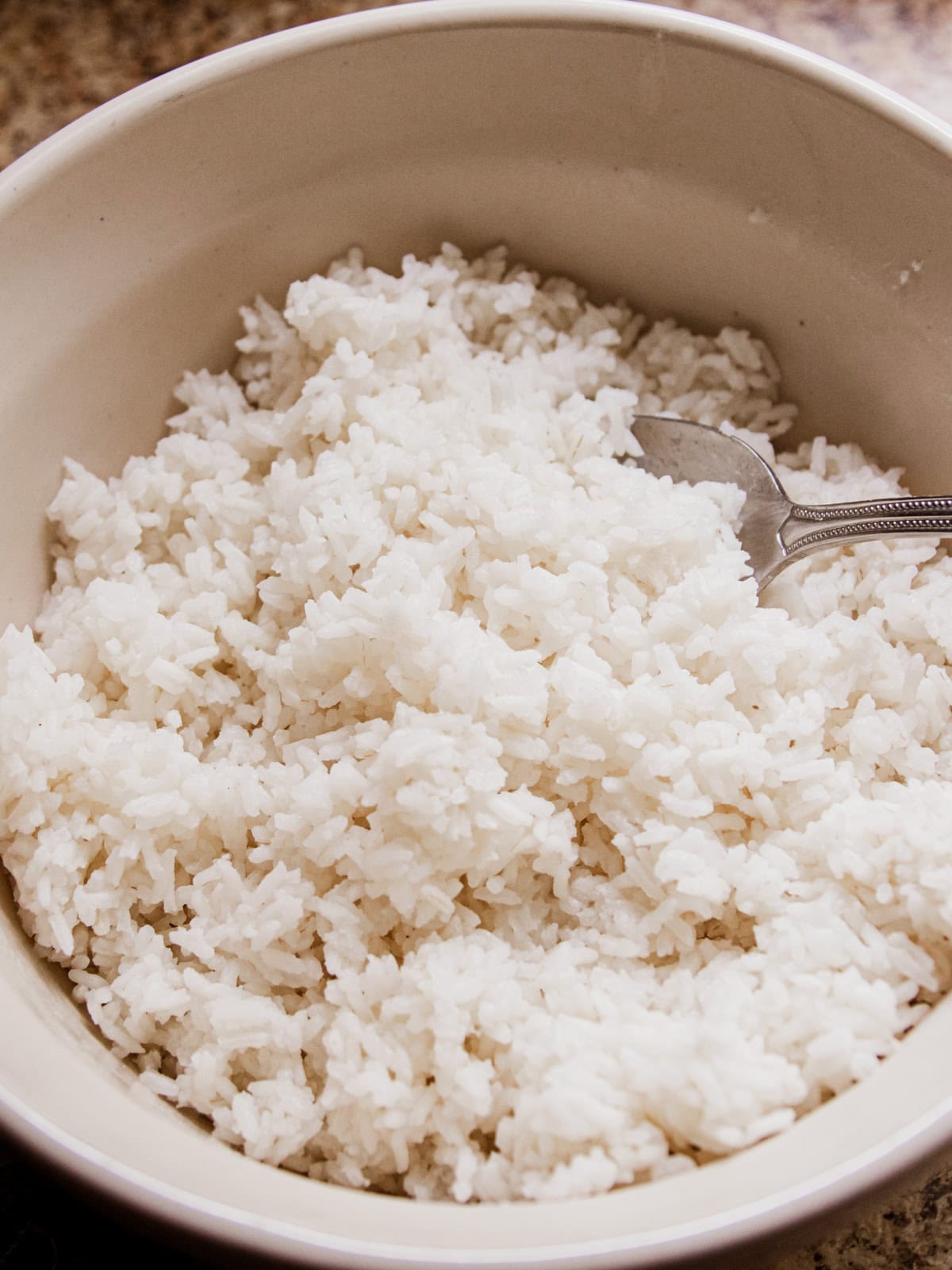 A white bowl filled with cooked white rice and a spoon.