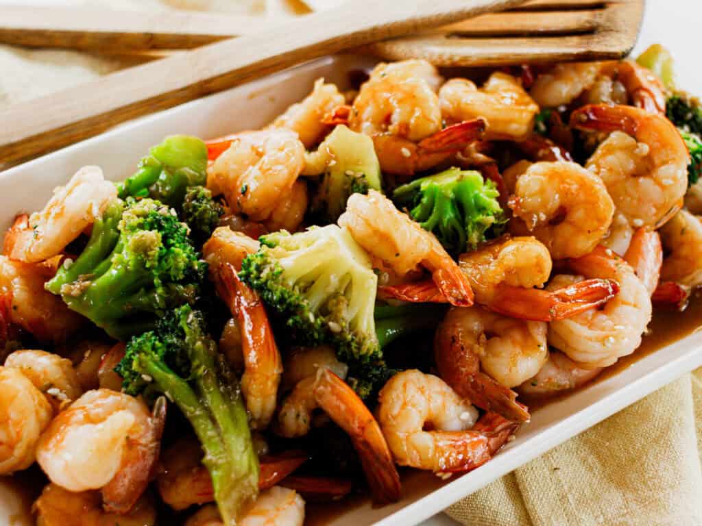 Shrimp and Broccoli Stir Fry on a white serving dish, with wooden serving utensils.