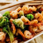 Shrimp and Broccoli Stir Fry on a white serving dish, with wooden serving utensils.