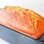 A loaf of whole wheat sweet bread in a bread pan on a white counter.