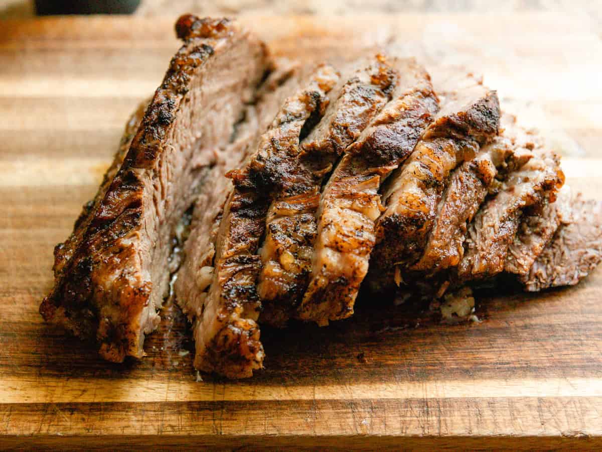 Thick sliced braised brisket on a wooden cutting board.