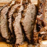 Braised brisket sliced into thick sections on a wooden cutting board.