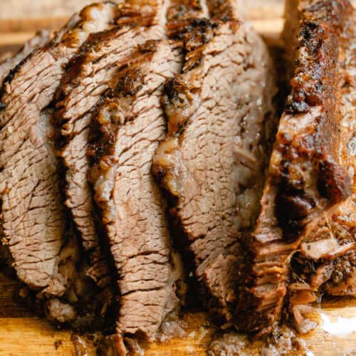 Braised brisket sliced into thick sections on a wooden cutting board.