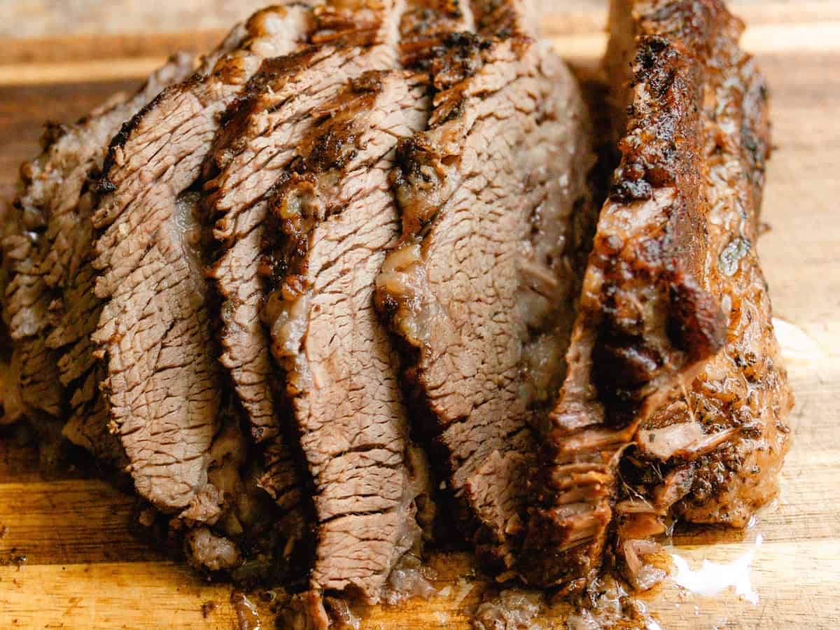 Braised brisket sliced into thick sections on a wooden cutting board.