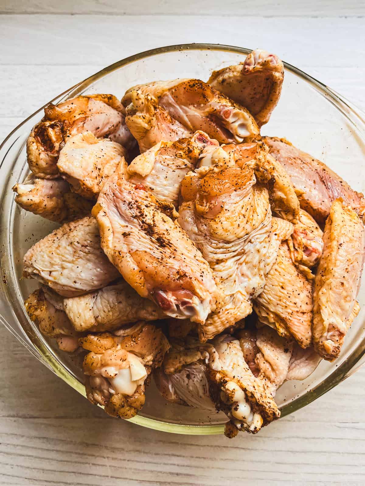 Unbaked chicken wings in a bowl with seasoning.
