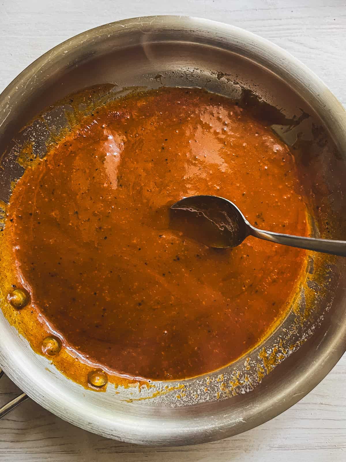 A pot of wing sauce being stirred with a spoon.