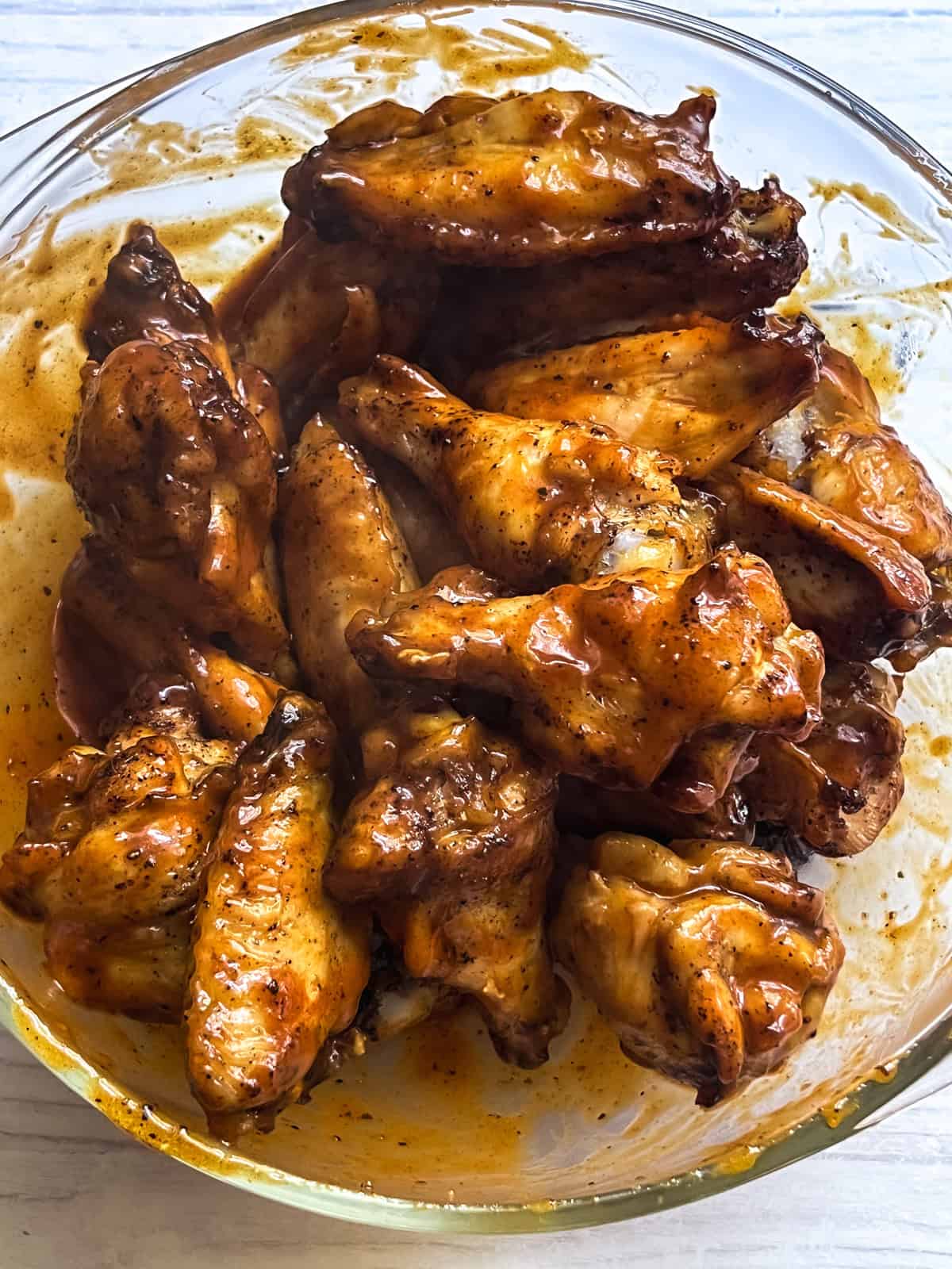 Homemade chicken wings tossed in sauce in a glass bowl.