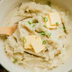 Dutch oven mashed potatoes in an enameled dutch oven with butter and chives on top.