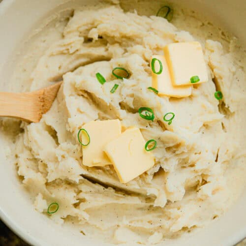 Dutch oven mashed potatoes in an enameled dutch oven with butter and chives on top.