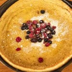 A dutch baby pancake in a cast iron skillet, with powdered sugar and berries on top.