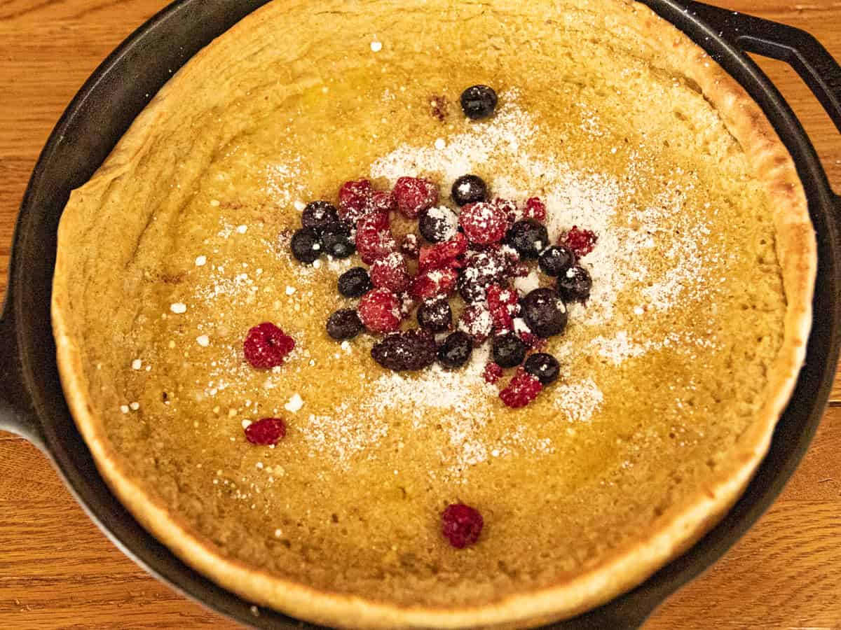 A dutch baby pancake in a cast iron skillet, with powdered sugar and berries on top.