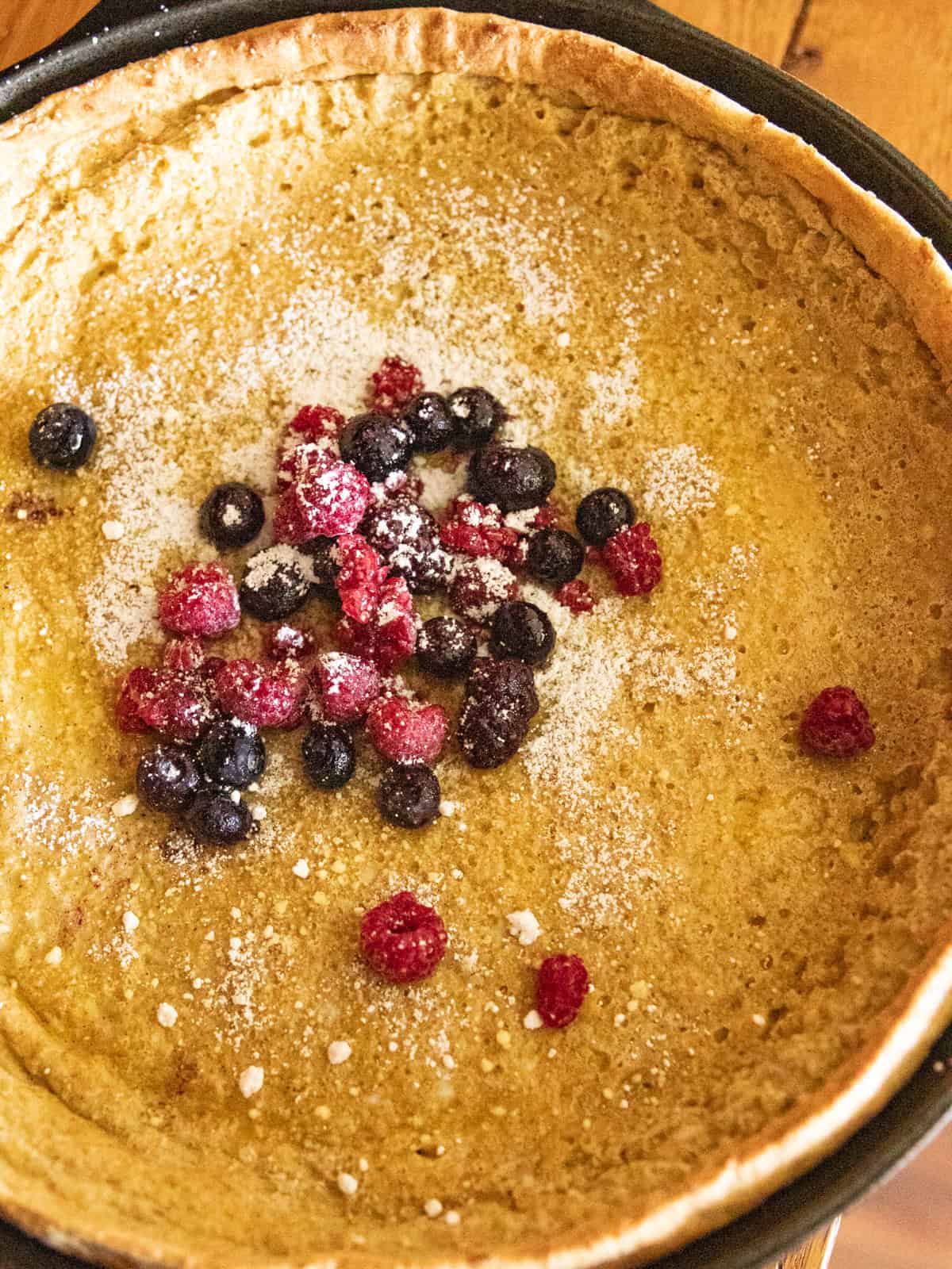 A dutch baby pancake in a cast iron skillet with powdered sugar and berries.