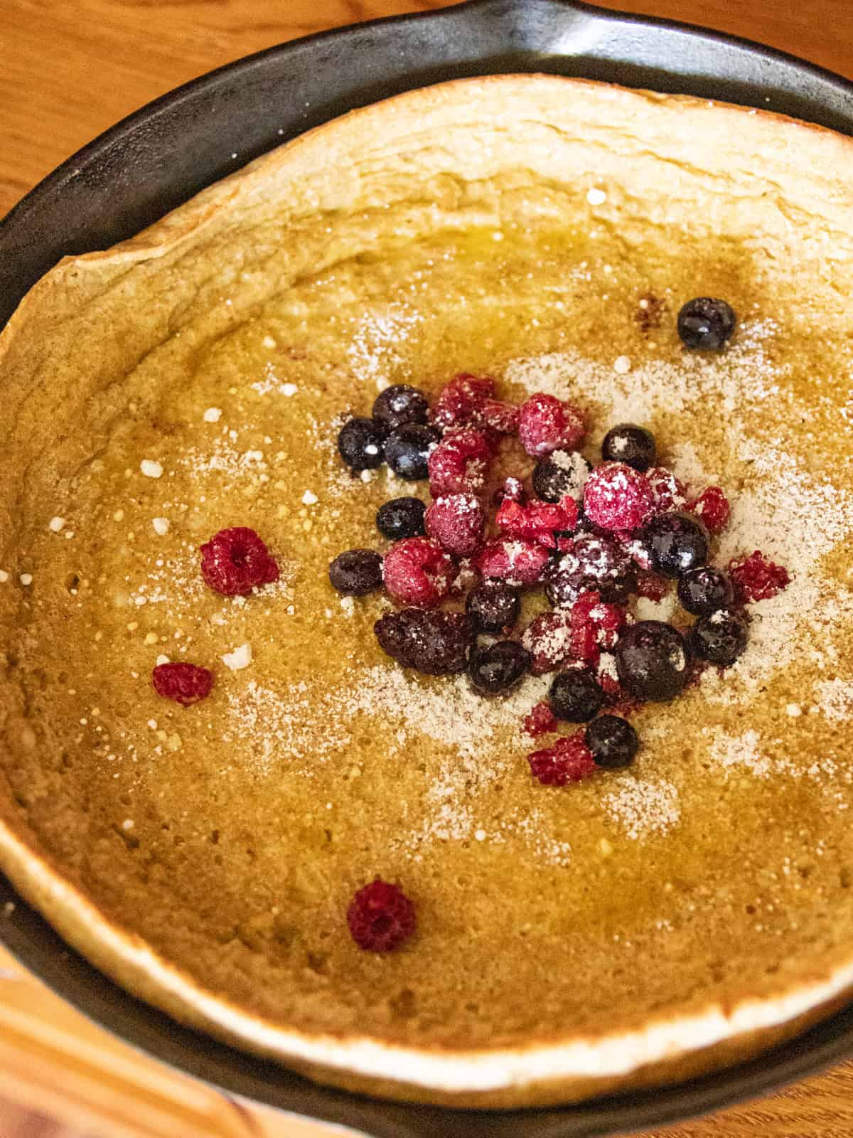 A dutch baby pancake with powdered sugar and berries in a cast iron skillet.