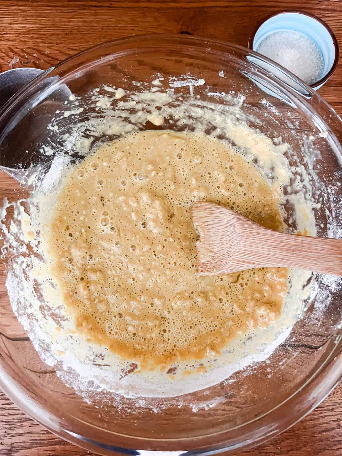 Eggs and flour in a glass bowl, being mixed with a wooden spoon.