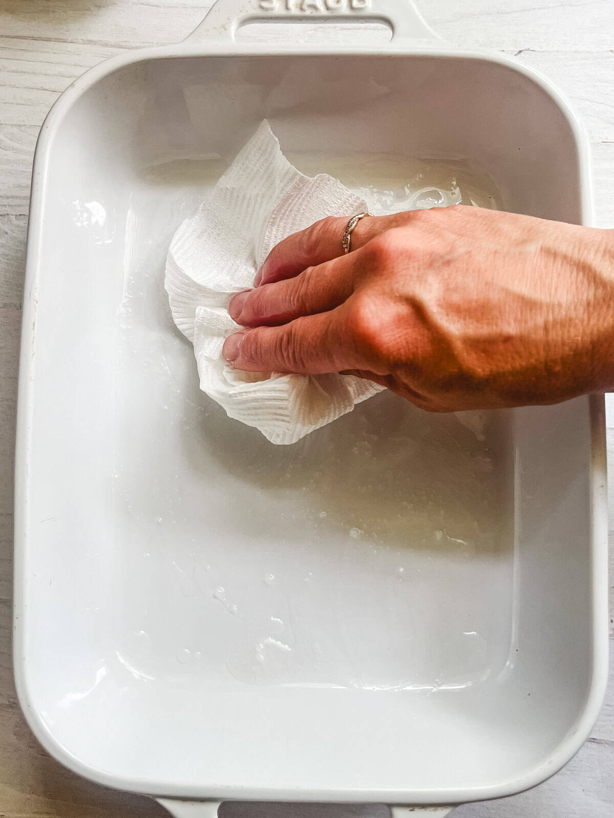 Greasing a baking dish by rubbing oil into it with a paper towel.