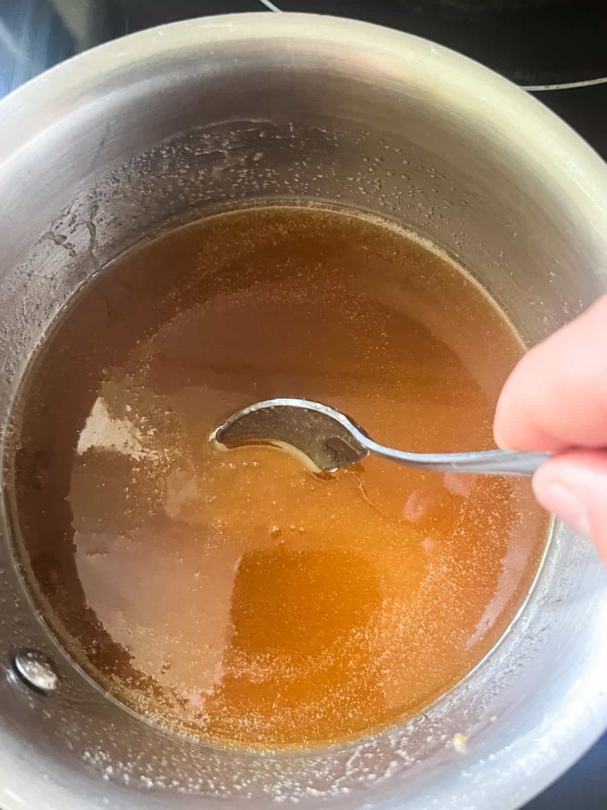 Stirring a saucepan with melted butter and brown sugar in it. 