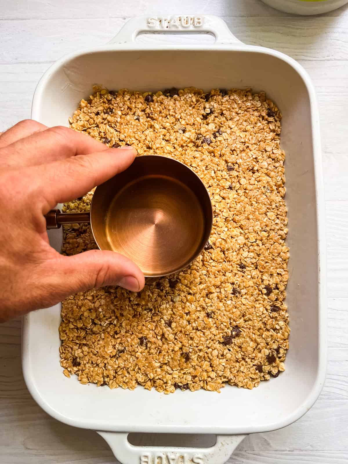 Pressing a measuring cup into homemade granola bars to press the oats together. 
