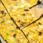 Serving a slice of sheet pan eggs out of a sheet pan with a wooden spatula.