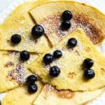Skillet crepes spread on a white plate and topped with fresh blueberries.
