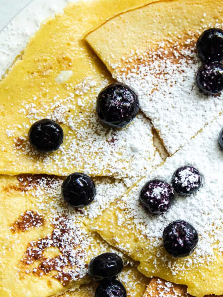 Skillet crepes on a white plate with fresh blueberries and powdered sugar.