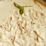 Alfredo sauce and pasta in a cast iron skillet with a sprig of basil on top.
