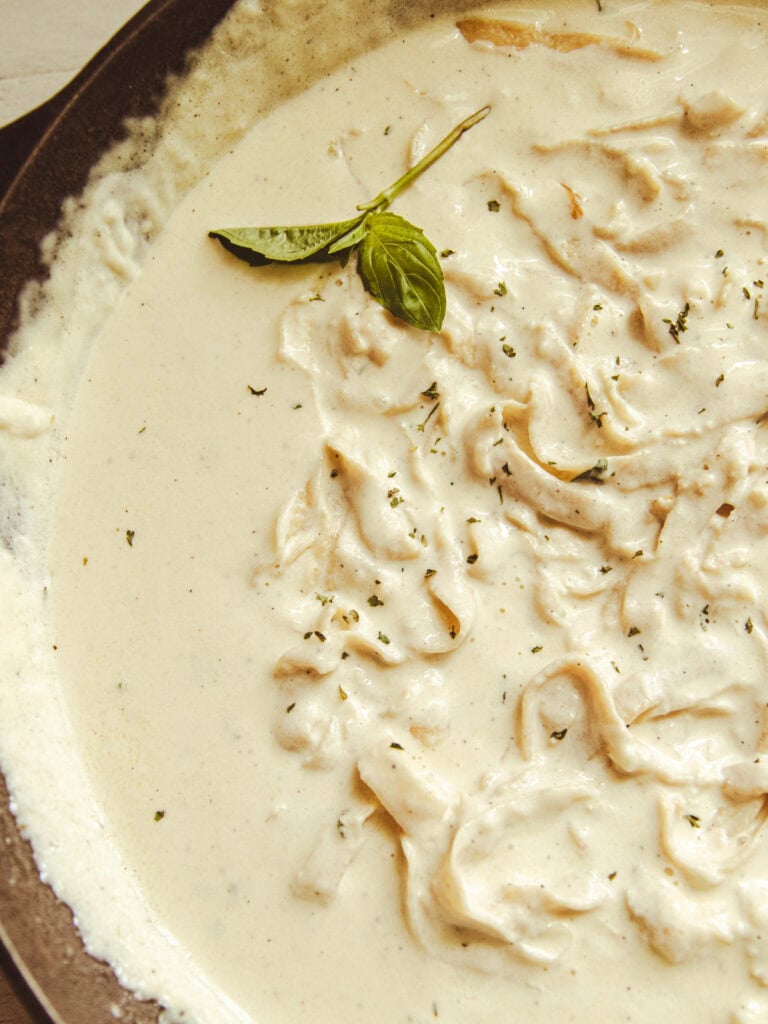 Homemade alfredo sauce and pasta in a serving dish with a sprig of basil on top.