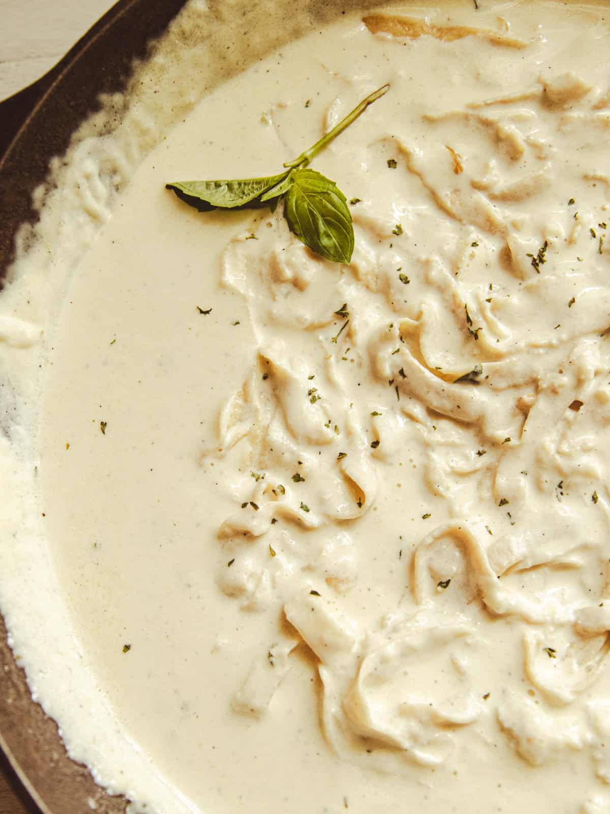 Homemade alfredo sauce and pasta in a serving dish with a sprig of basil on top.