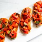 Balsamic bruschetta lined up on a white platter.