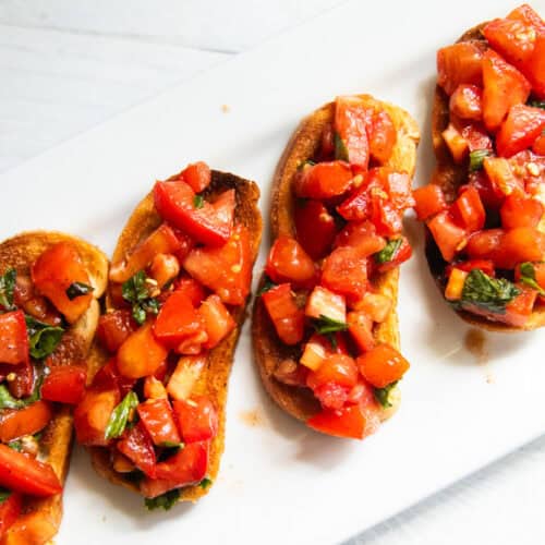 Balsamic bruschetta lined up on a white platter.