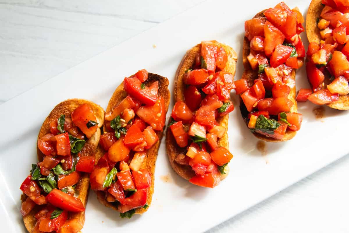 Balsamic bruschetta lined up on a white platter.