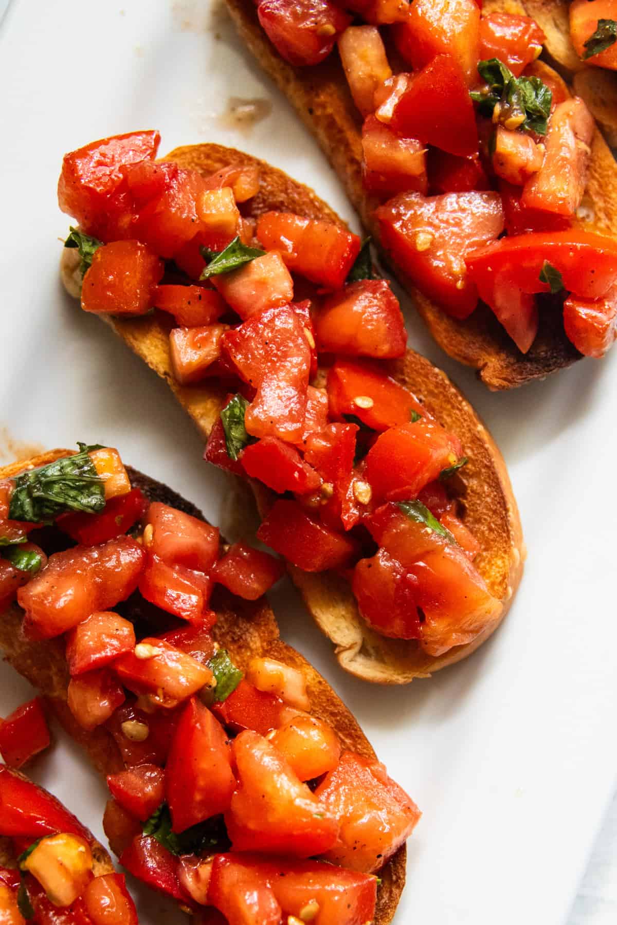 Three pieces of balsamic bruschetta laying diagonally on a white plate.
