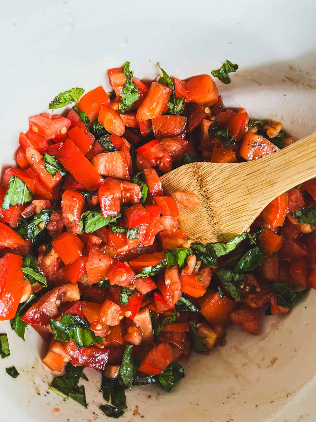 Stirring a bowl of bruschetta topping with a wooden spoon.